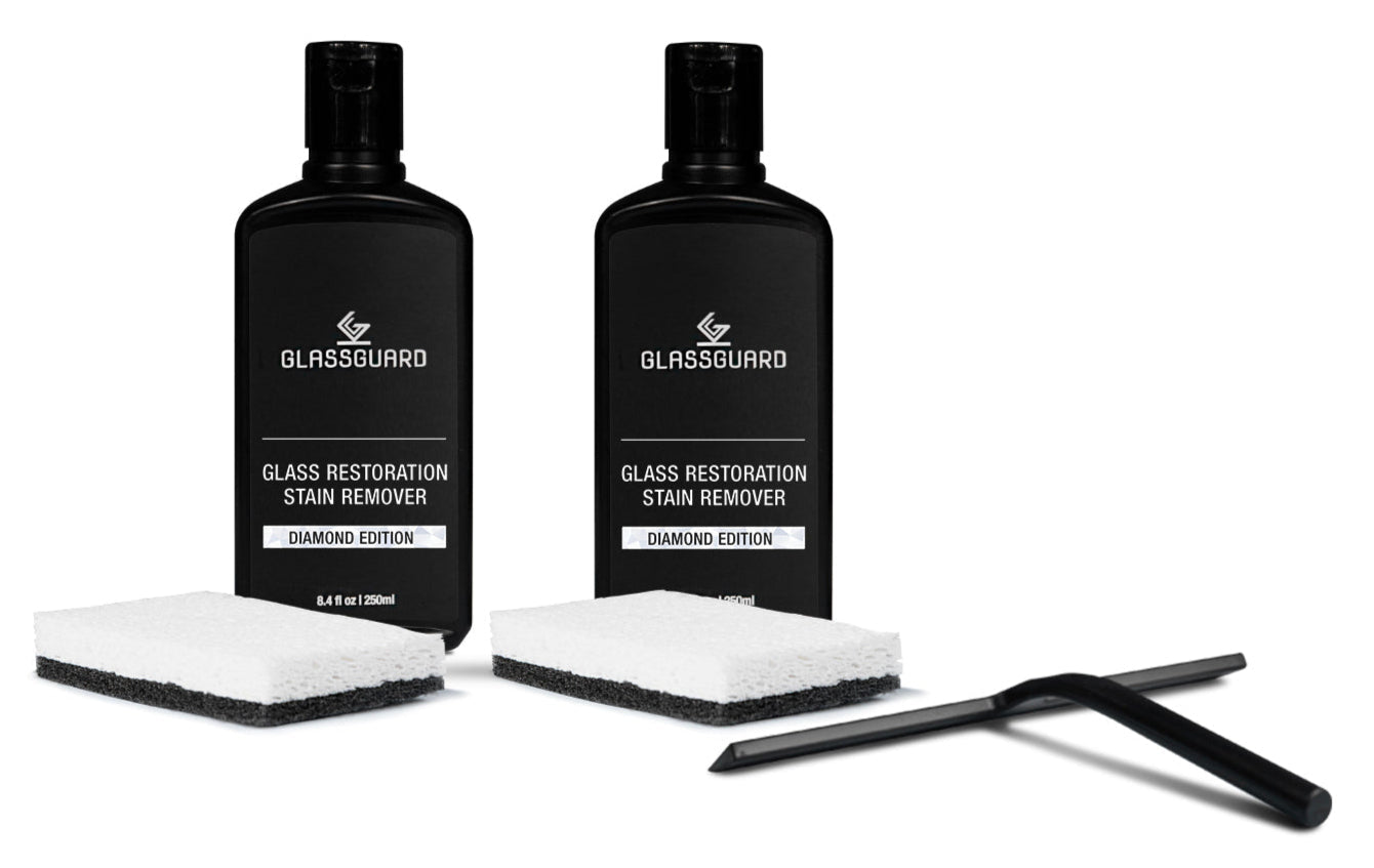 Two bottles of Glassguard Glass Restoration Stain Remover with sponges and a black squeegee