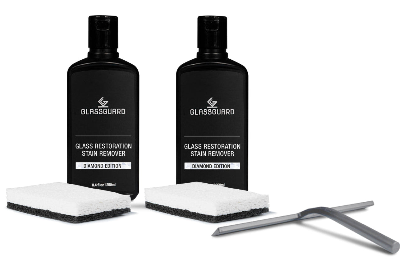Two bottles of Glassguard Glass Restoration Stain Remover with sponges and a grey squeegee